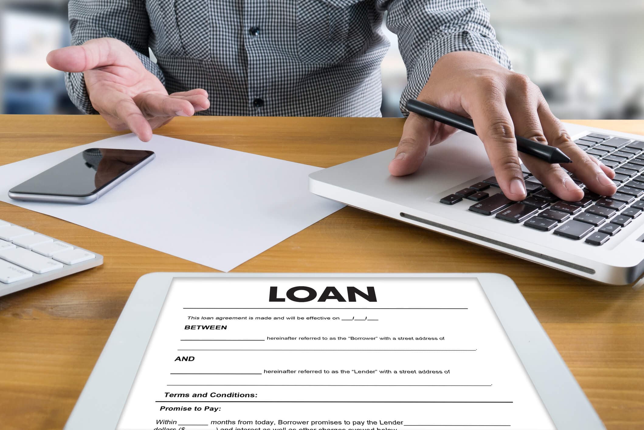 A borrower reviews a loan agreement while using a laptop at a desk. The image represents comparing signature loans and personal loans, including borrowing costs, repayment terms, qualification requirements, and other factors to consider before accepting a loan.
