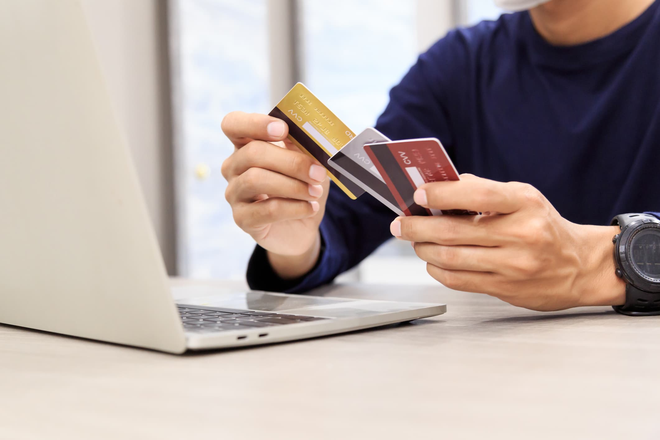 Person holding multiple credit cards while using a laptop, symbolizing financial management and Arro credit card use.