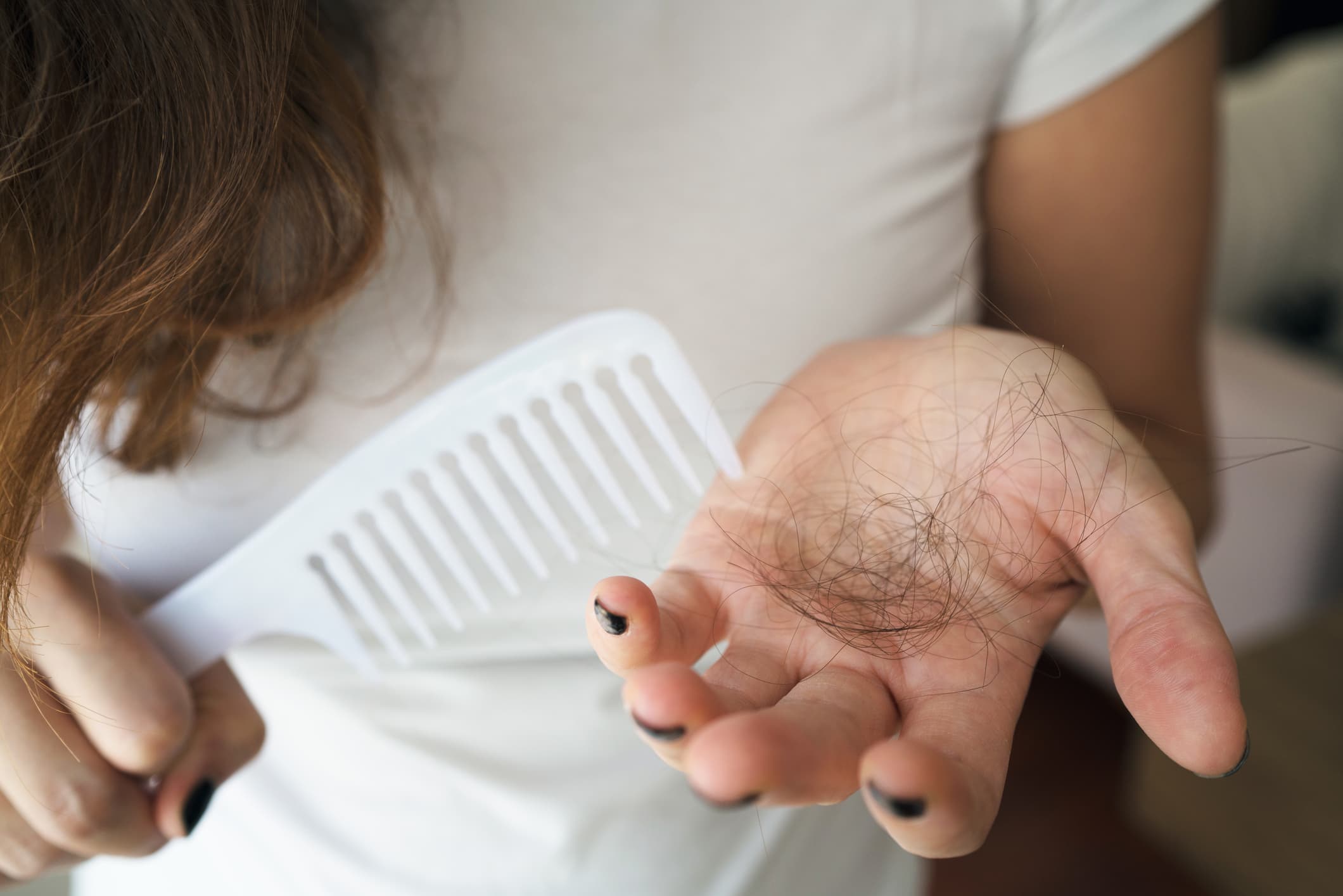Woman holding hair shed in her hand while combing, illustrating concerns addressed by the best hair loss treatments