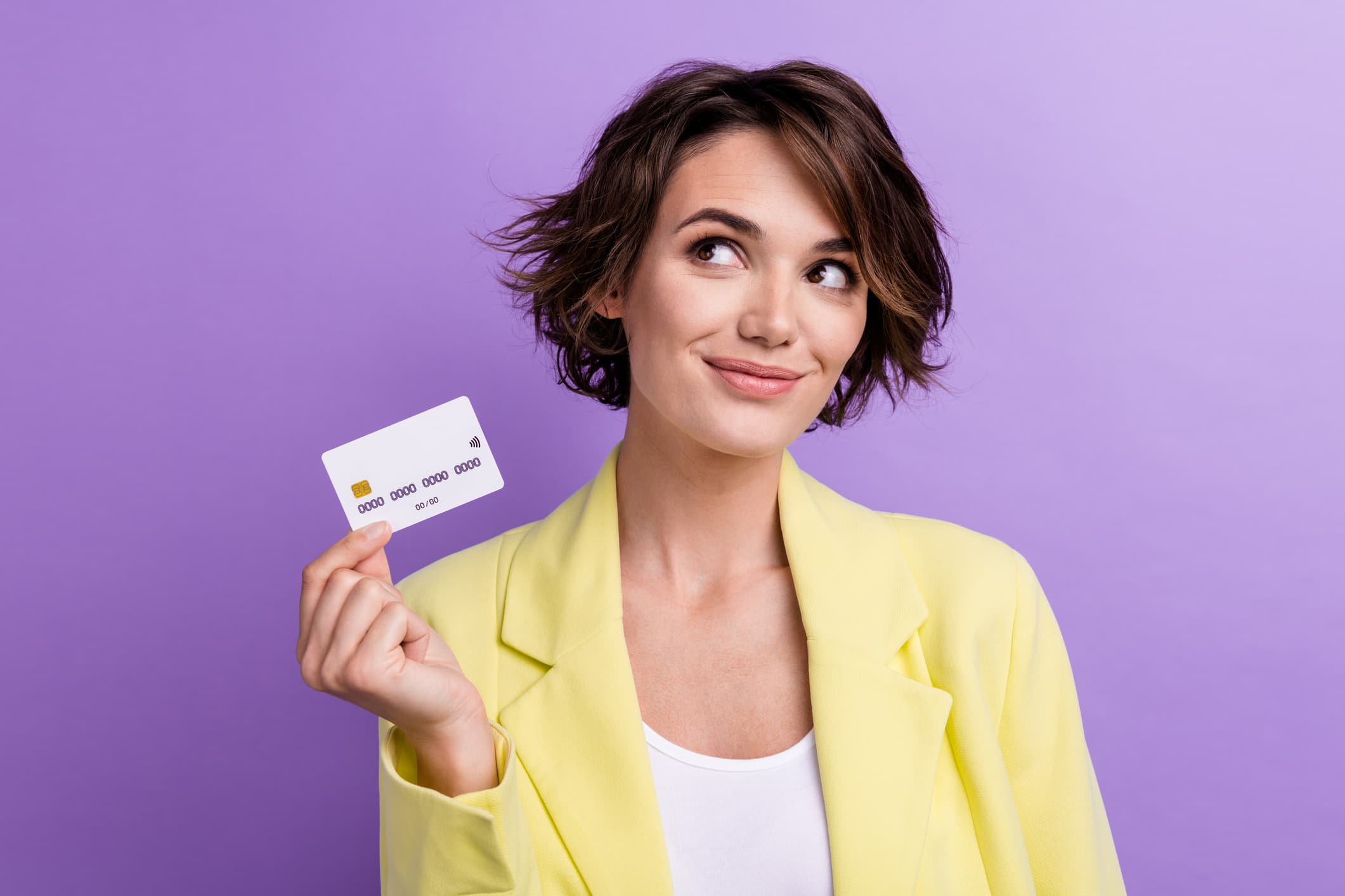 Smiling woman in a bright yellow blazer holding a white credit card, symbolizing positive Imagine Visa credit card reviews.