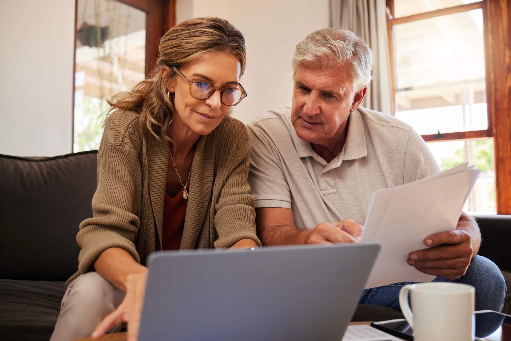 A couple reviews financial paperwork together at home while using a laptop, representing HSA planning, healthcare savings, and preparation for future medical expenses.