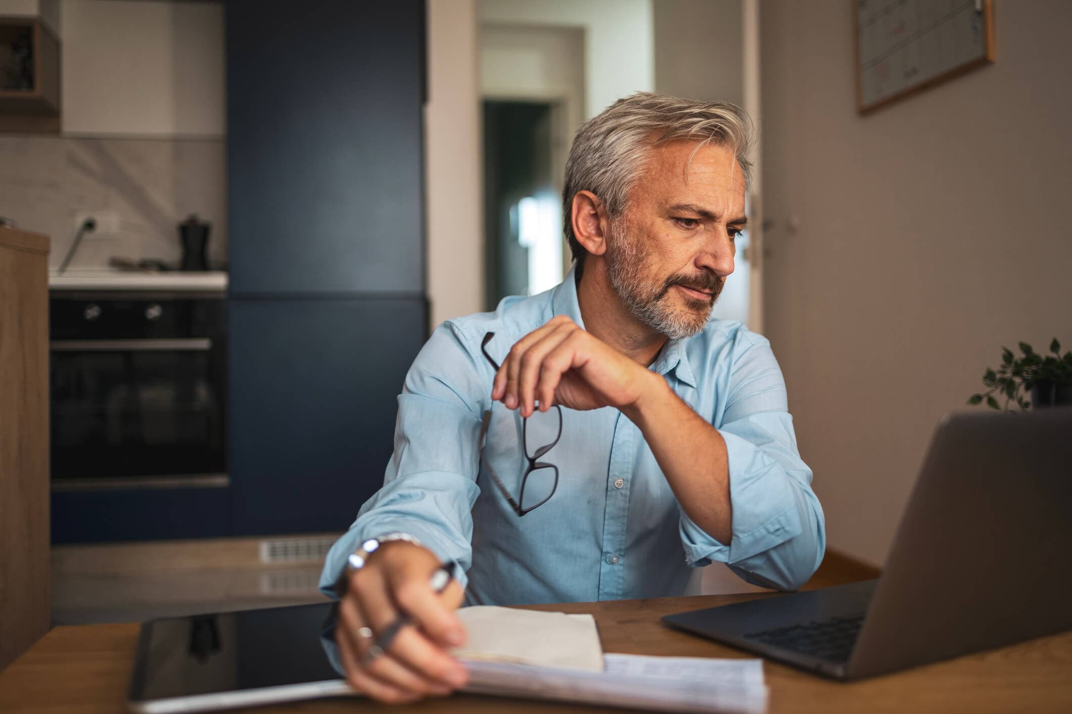 A man reviews financial information on his laptop and paperwork at home. Debt consolidation can affect credit in several ways, making it important to understand the potential short- and long-term impact before consolidating debt.