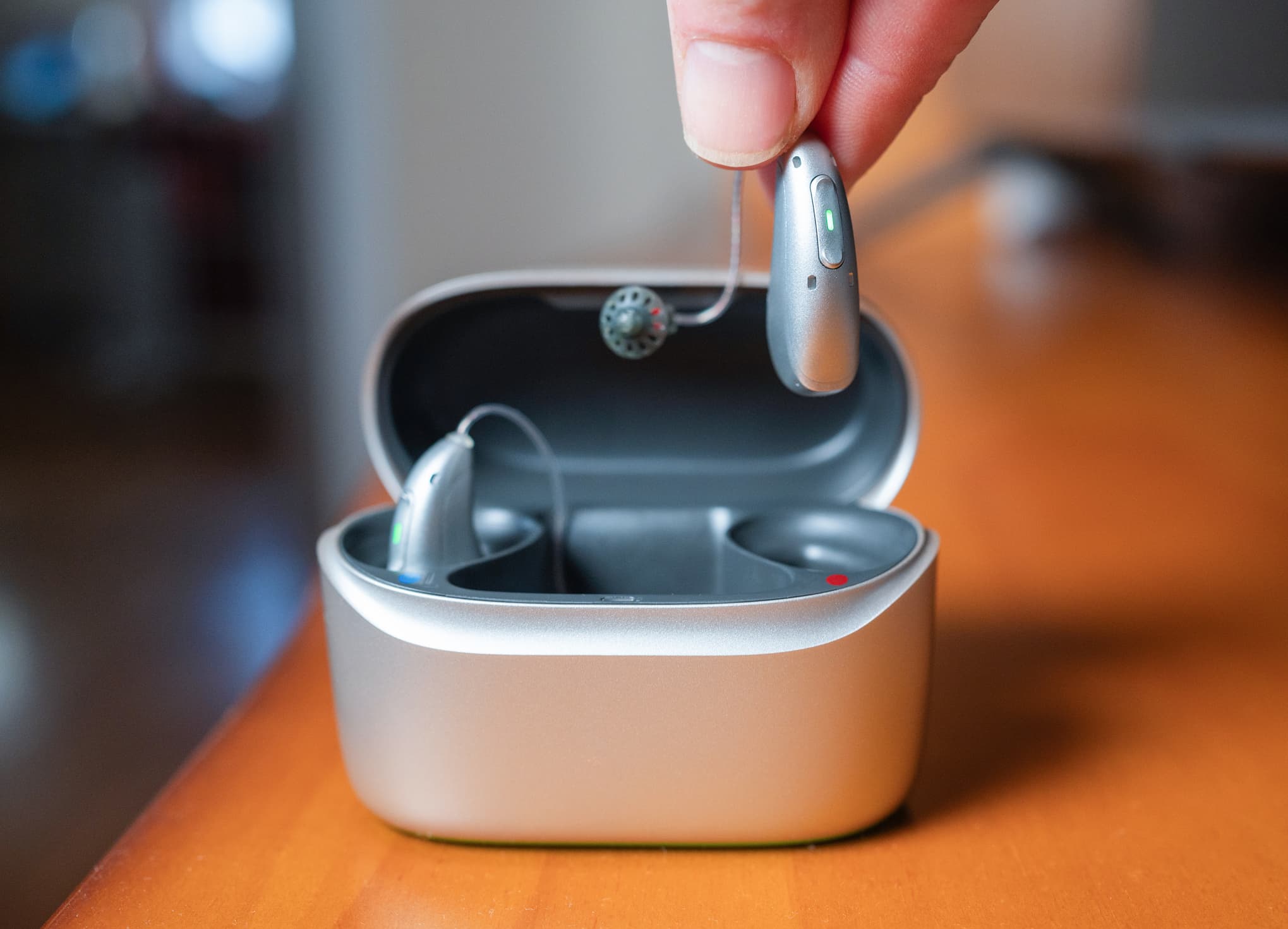 Close-up of affordable rechargeable hearing aids being removed from a charging case, illustrating modern low-cost hearing aid technology.