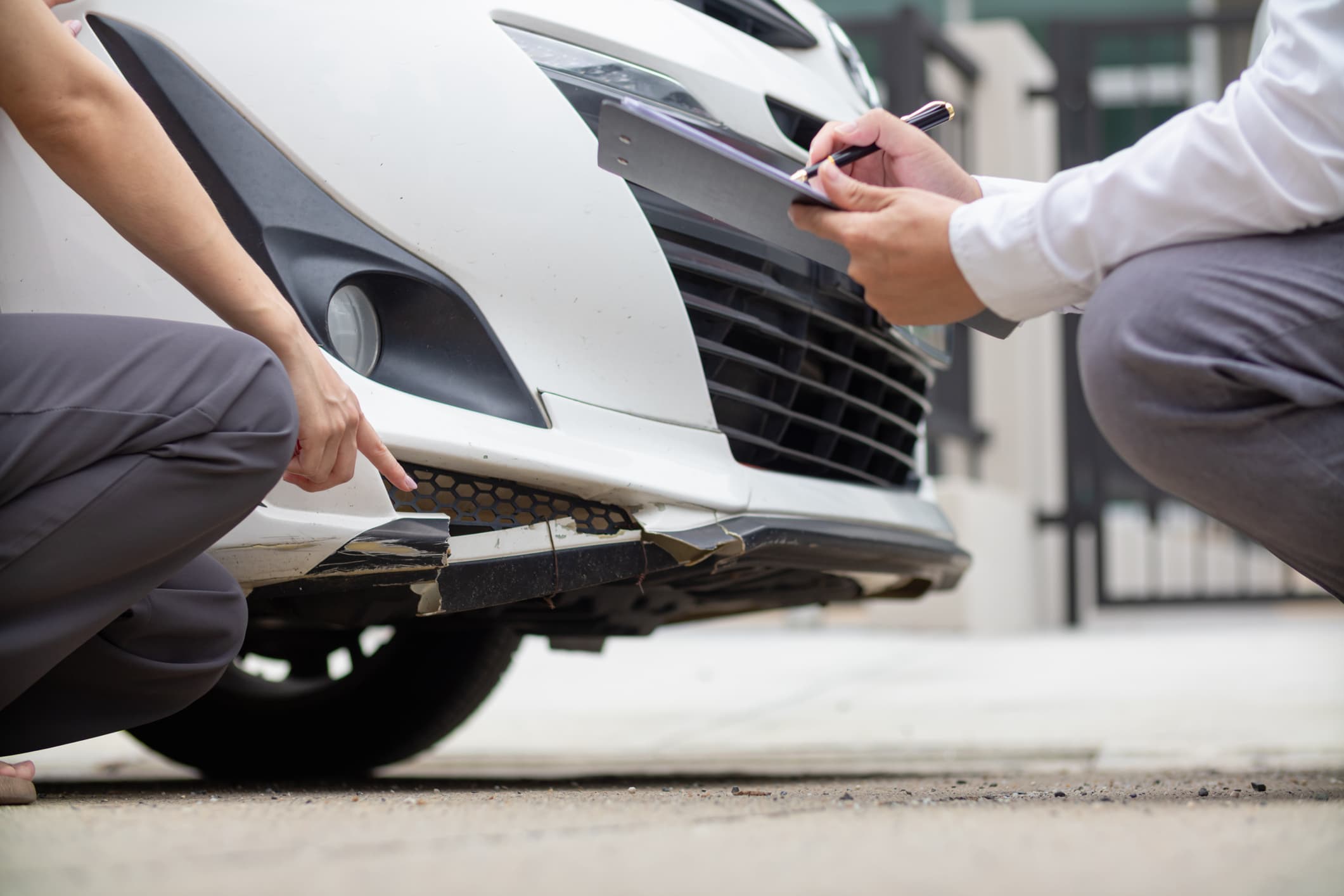 Insurance agent inspecting bumper damage on a white car, representing State Farm car insurance reviews and claims process.