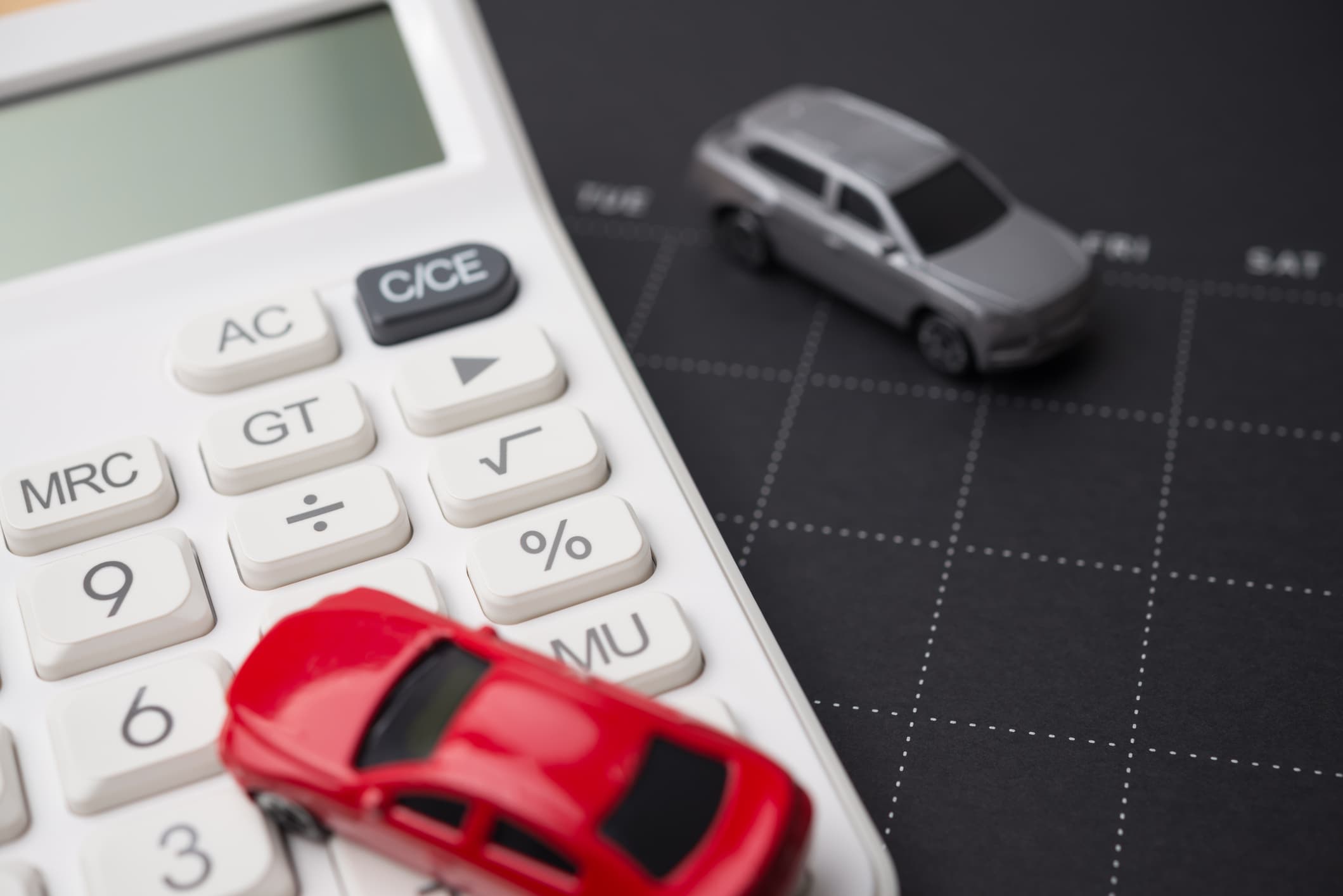 Calculator with toy cars on a calendar background representing Capital One Auto Finance auto loan planning