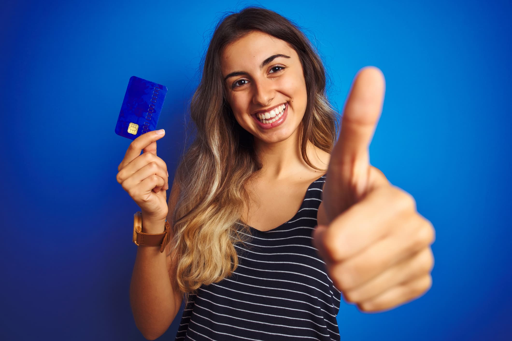 Smiling woman holding a blue credit card and giving a thumbs up — best credit card for good credit