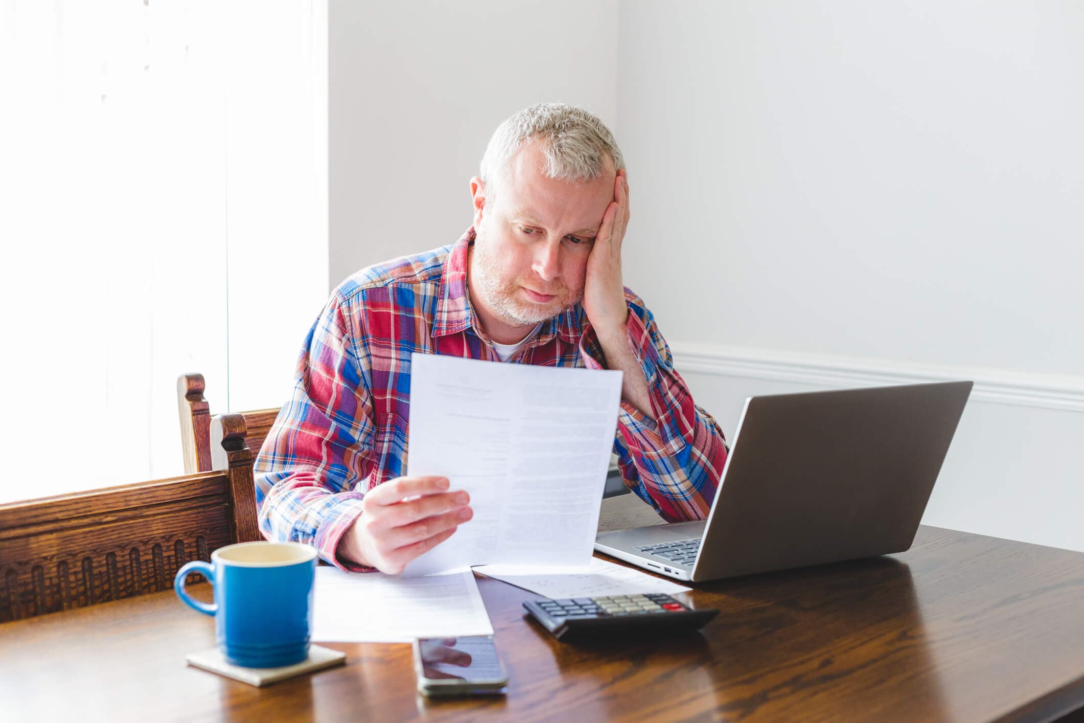 A man reviews bills and financial documents at home while using a laptop and calculator, illustrating the stress that can come with unpaid credit card debt and potential collection action.