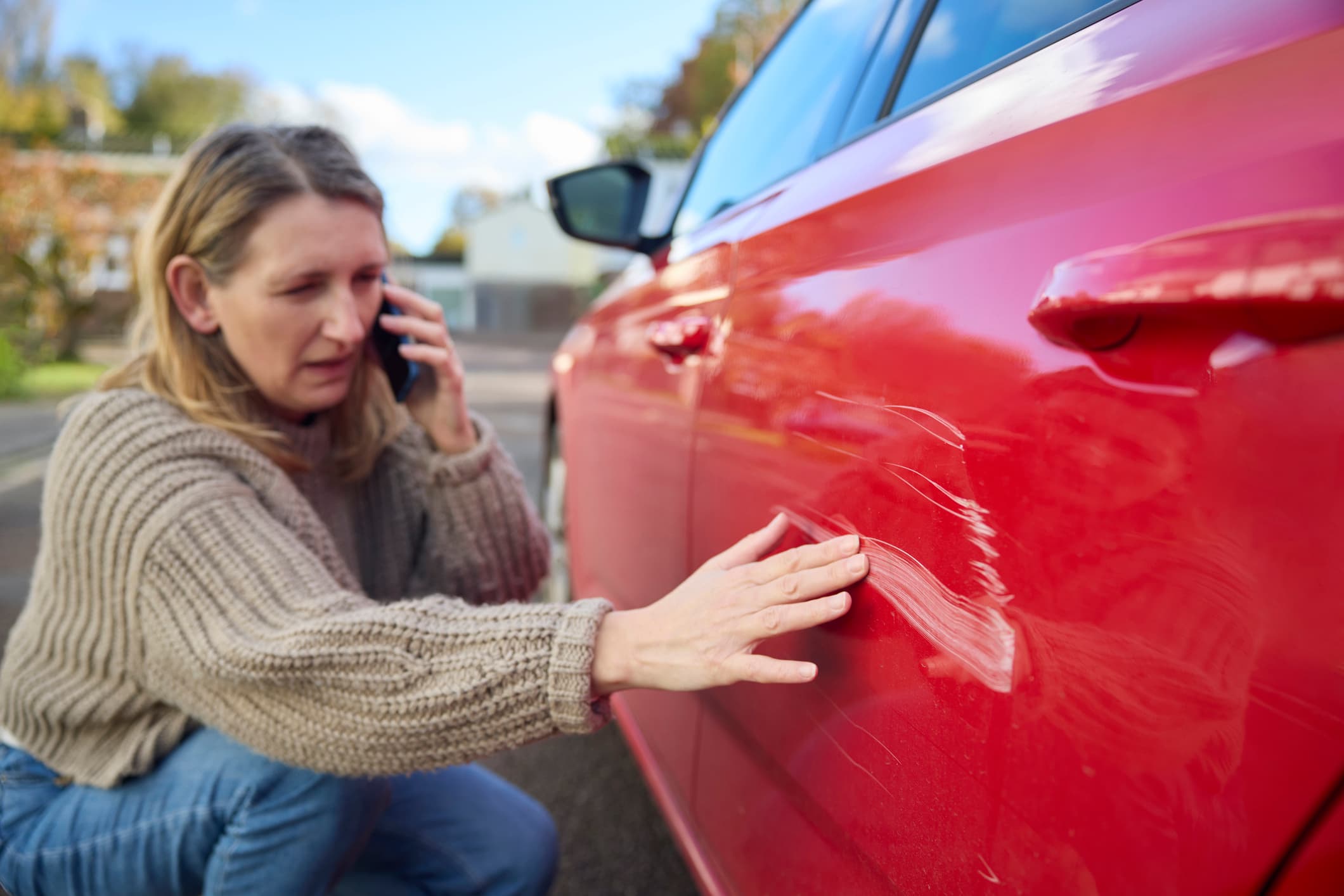 Woman on phone inspecting car damage, representing Auto-Owners car insurance and the claims process.