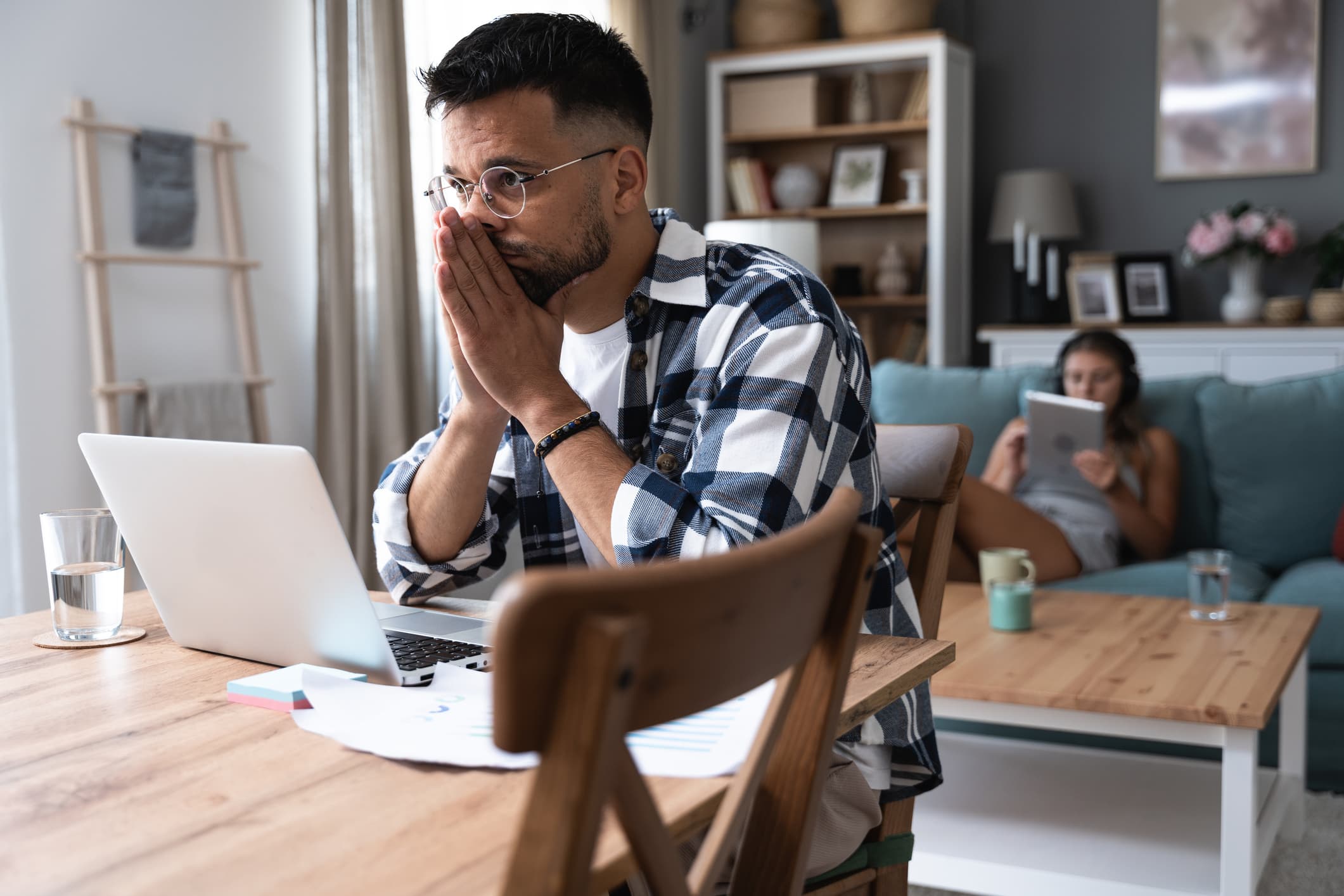 Man in a plaid shirt looking concerned while reviewing financial documents on a laptop, symbolizing research for above lending reviews.