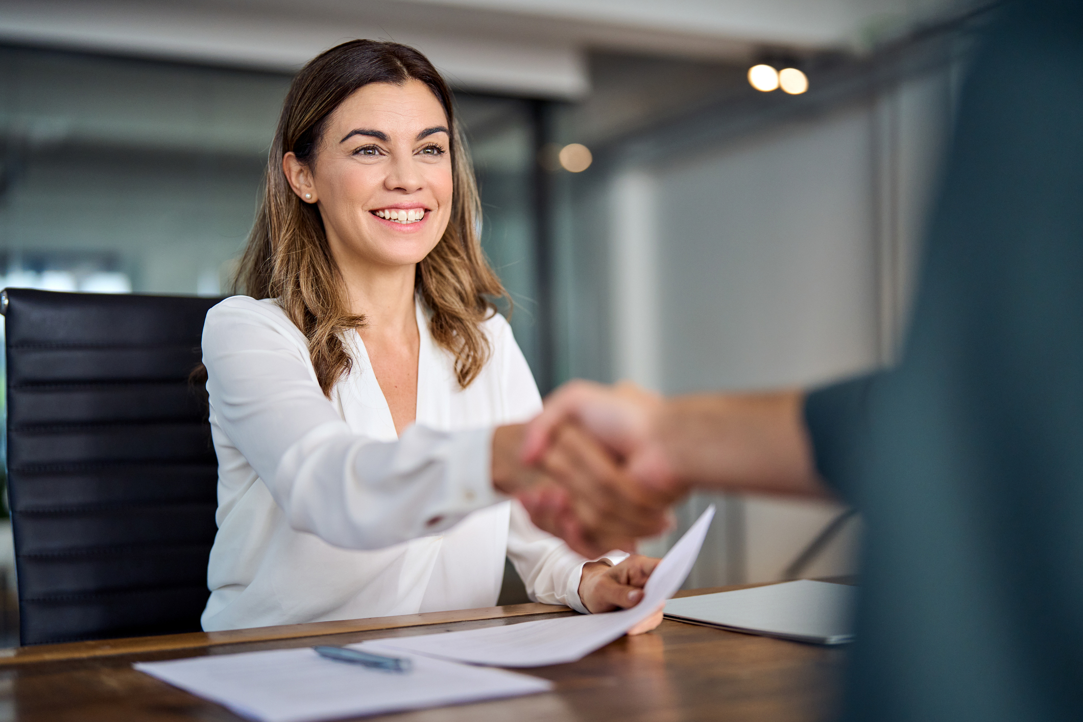 Smiling businesswoman shaking hands across a desk, sealing a successful business agreement or partnership. Fundbox review feature image