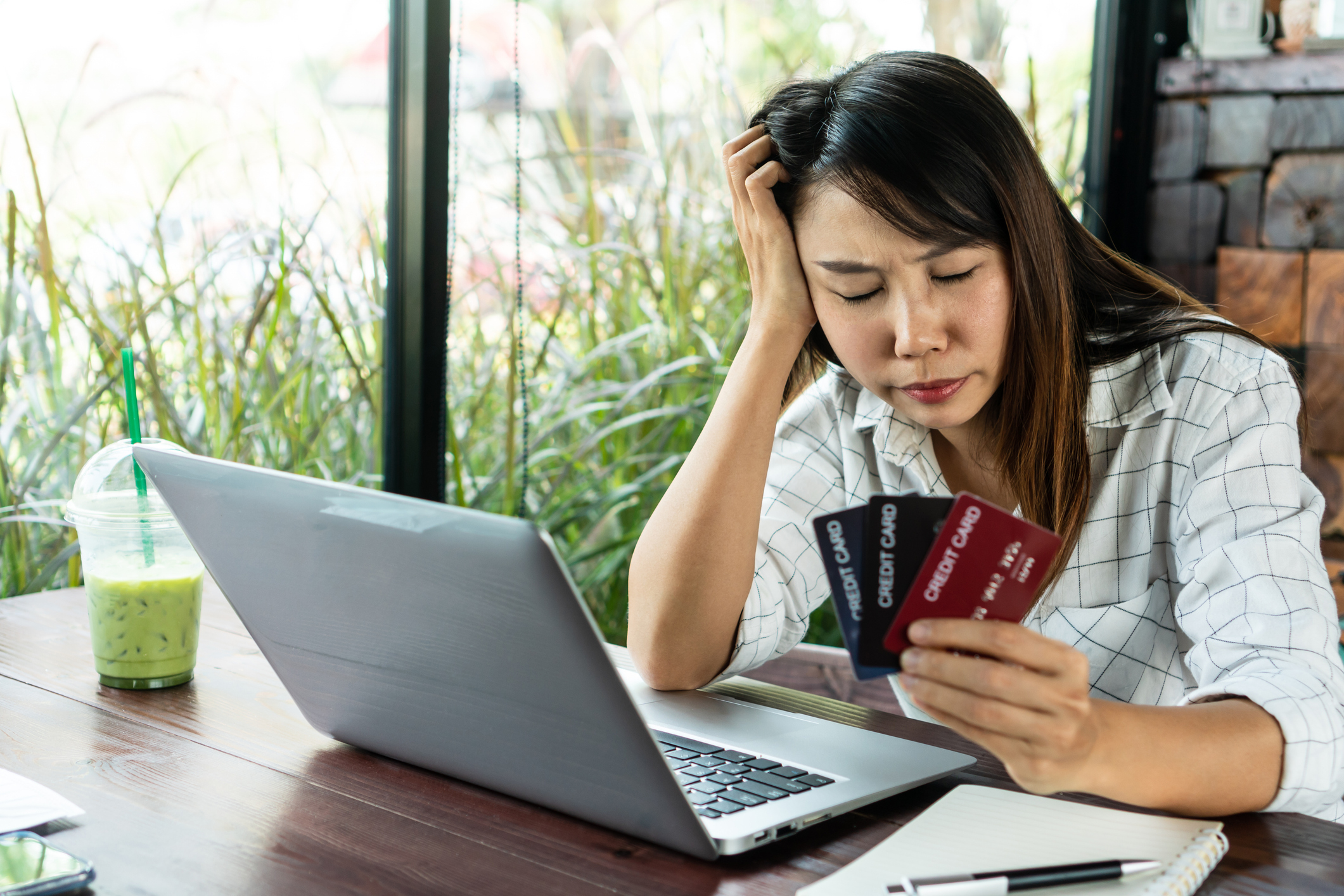 Worried woman holding multiple credit cards while looking at a laptop, symbolizing financial stress and debt review for amone review.