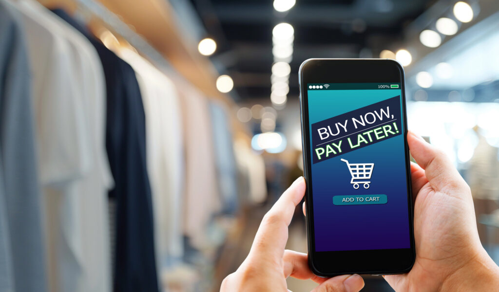 A realistic, horizontal image depicting a person using a smartphone to make a purchase, symbolizing the convenience of buy now, pay later apps.