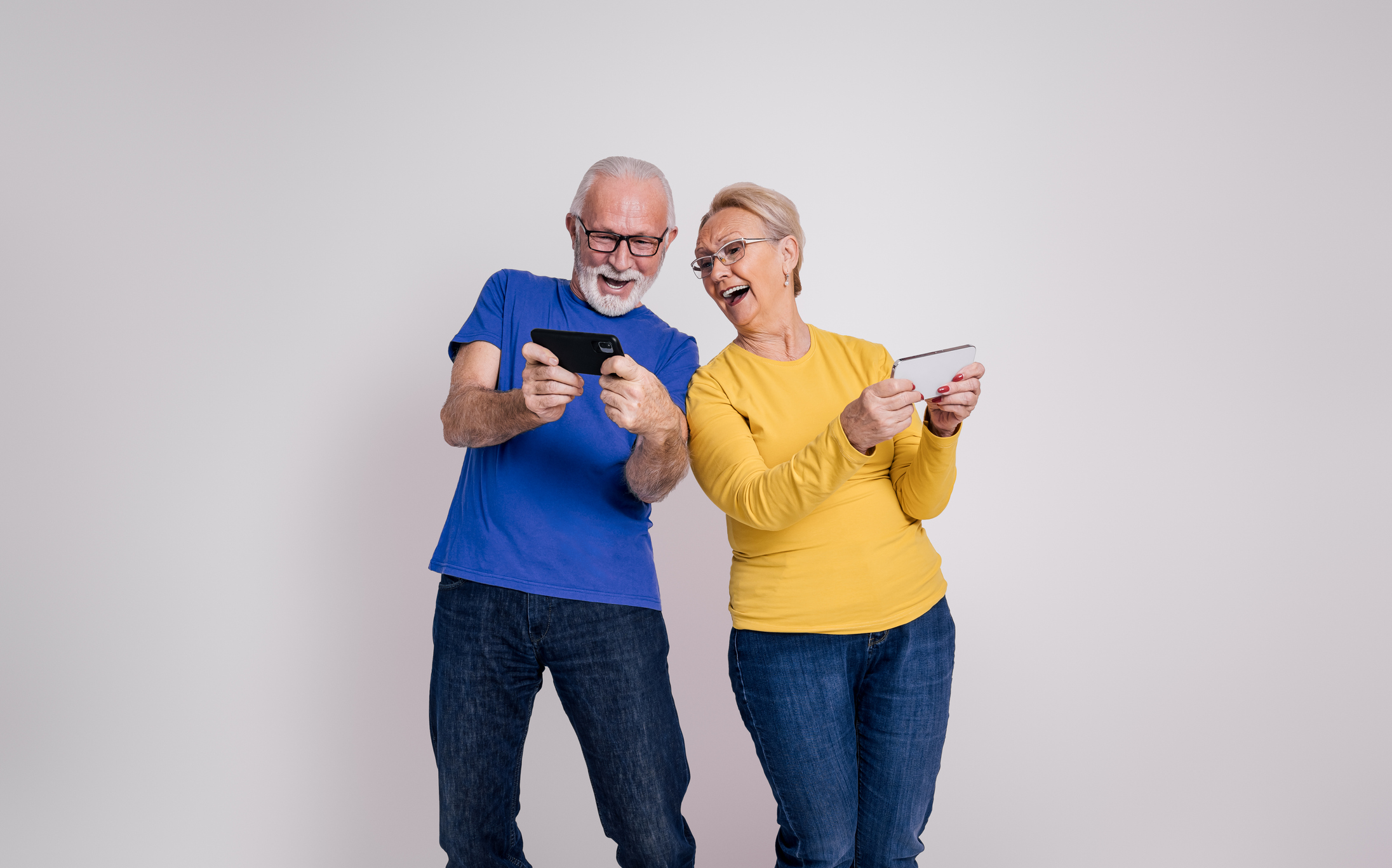 Smiling senior couple playing on smartphones, enjoying interactive apps for seniors that support fun and cognitive engagement.