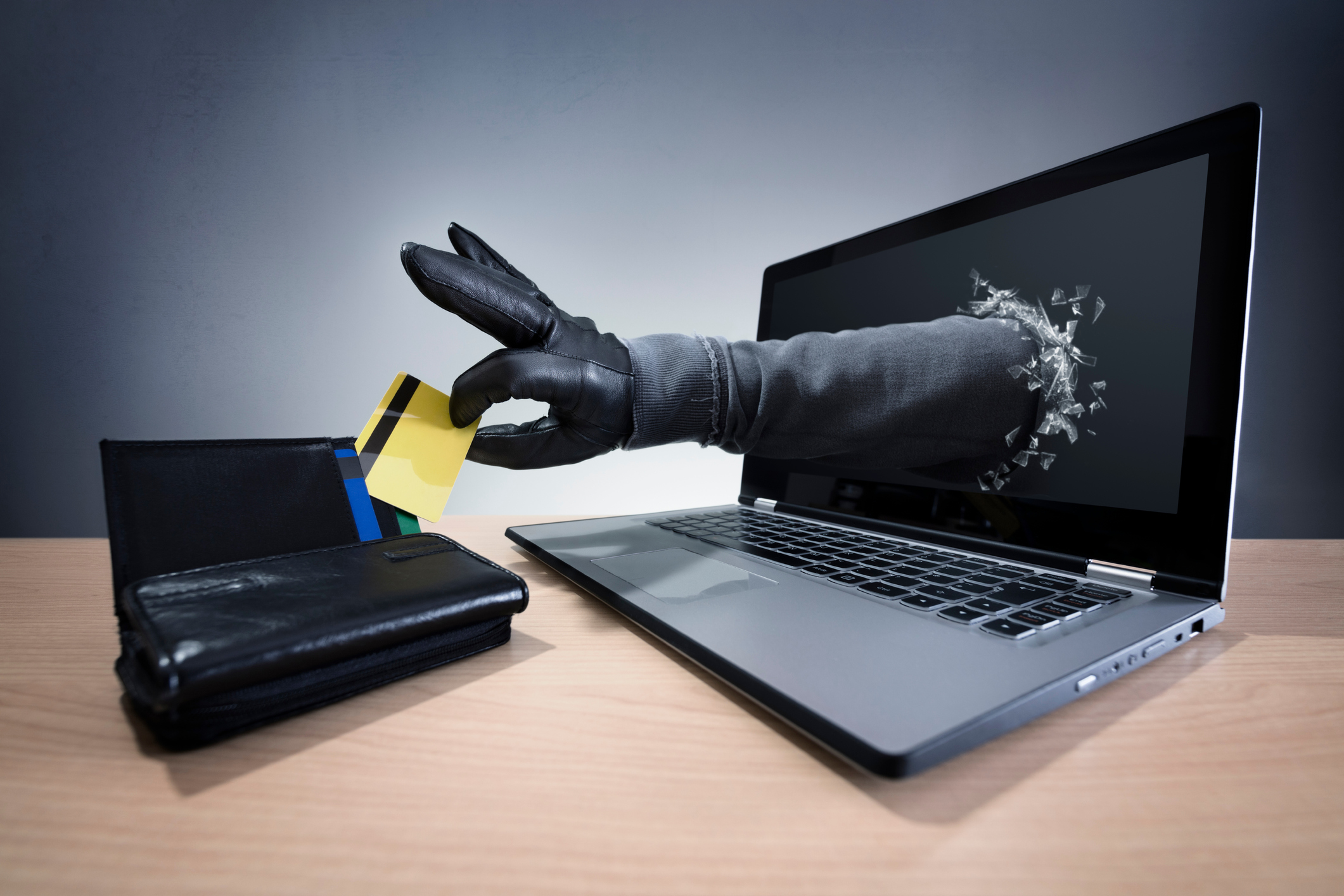 Do I need ID theft protection? A gloved hand reaches through a laptop screen to steal a credit card from a wallet, symbolizing online identity theft.
