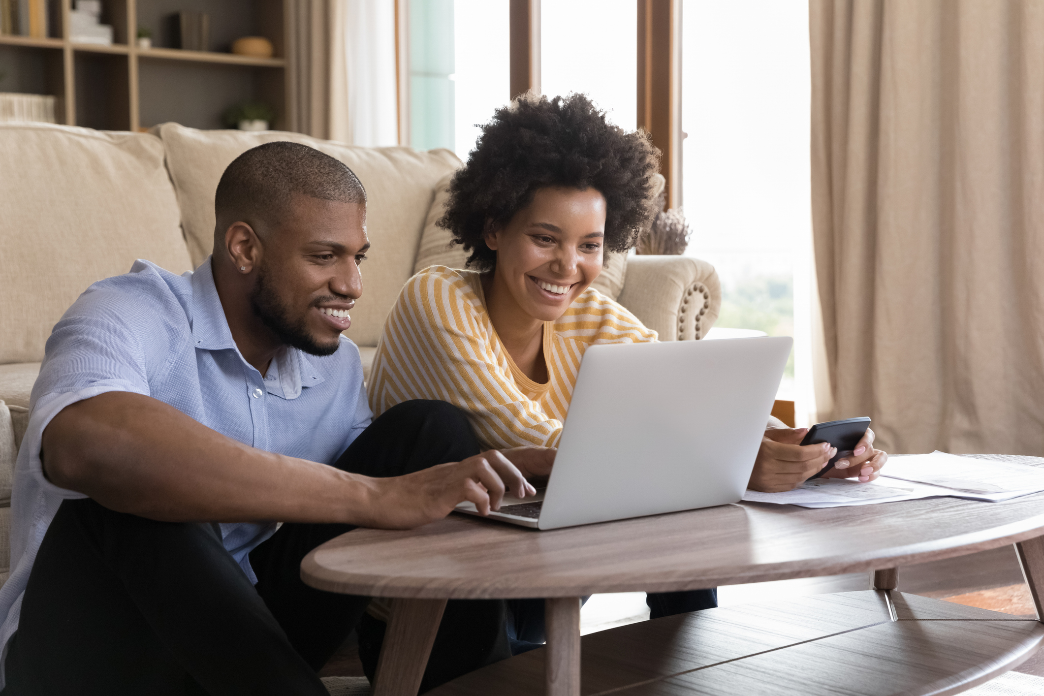 Smiling couple reviewing Rocket Mortgage reviews online using a laptop and smartphone in their living room