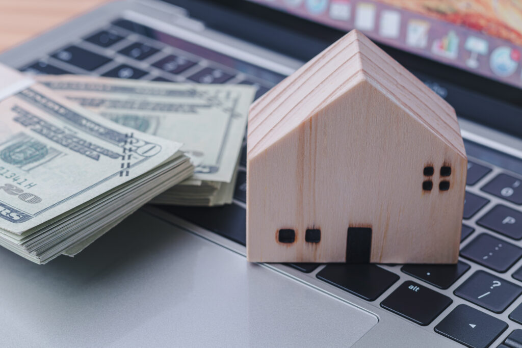 A stack of cash and a small wooden house model on a laptop keyboard, symbolizing digital lending and home equity access, for Figure home equity loan reviews.