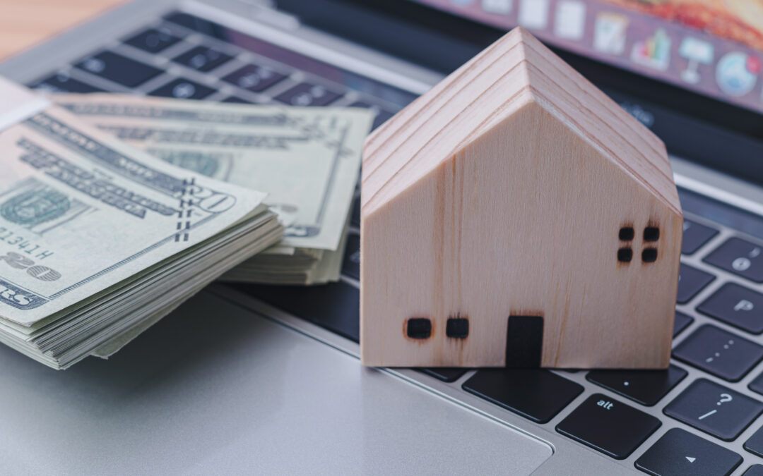 A stack of cash and a small wooden house model on a laptop keyboard, symbolizing digital lending and home equity access, for Figure home equity loan reviews.