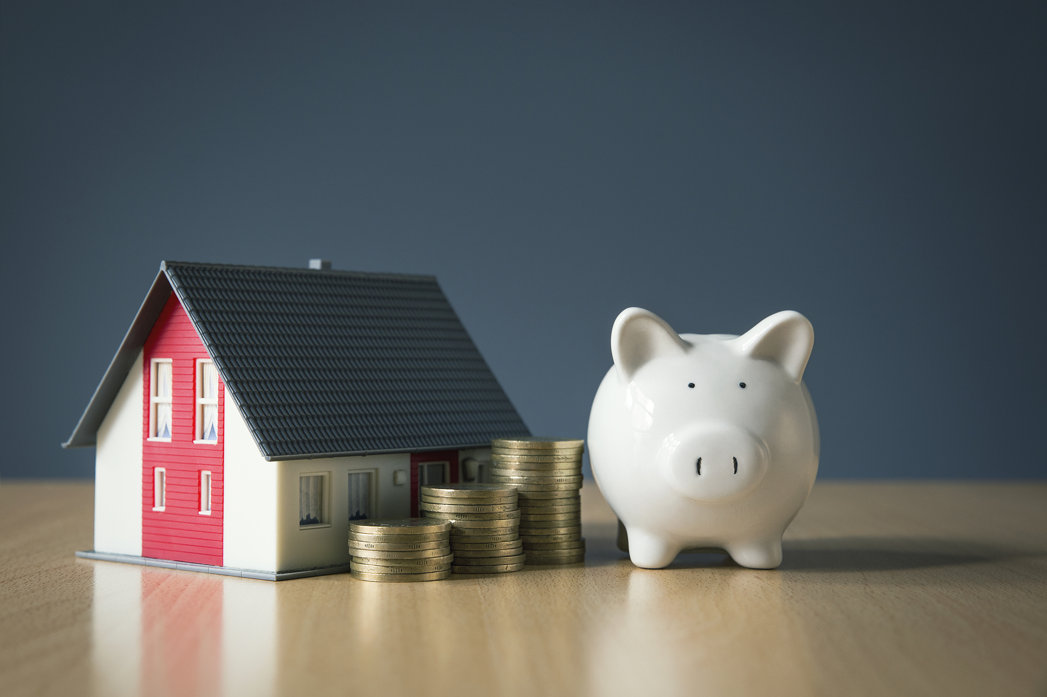 A model house, stacked coins, and a white piggy bank on a table, symbolizing home value and savings, representing the concept: can you take equity out of your home without refinancing?