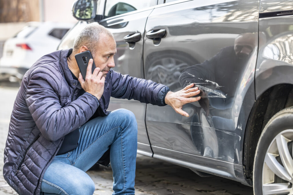 Man inspecting car damage while calling insurance after an accident, representing Lemonade car insurance reviews.