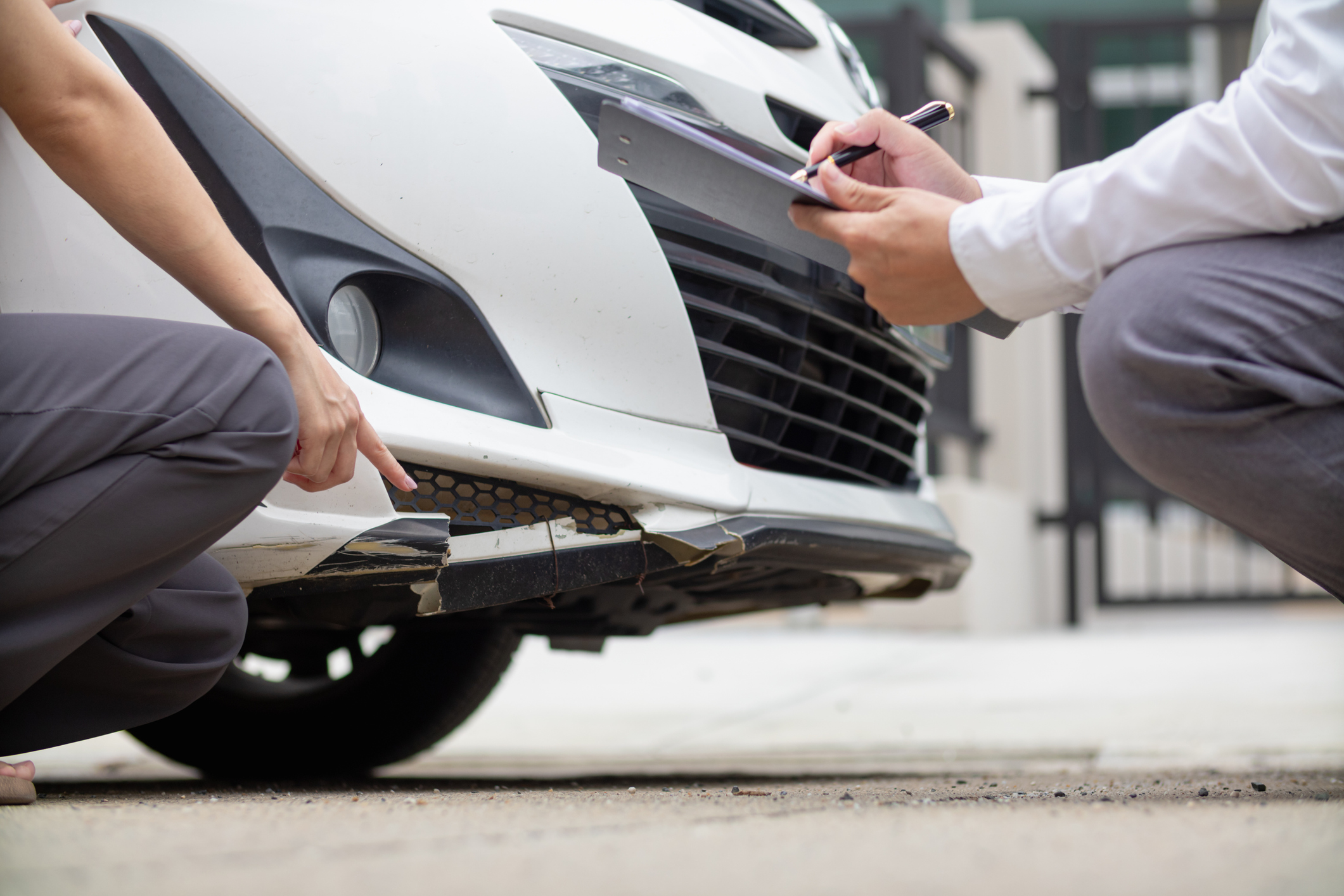 Insurance agent inspecting bumper damage on a white car, representing State Farm car insurance reviews and claims process.