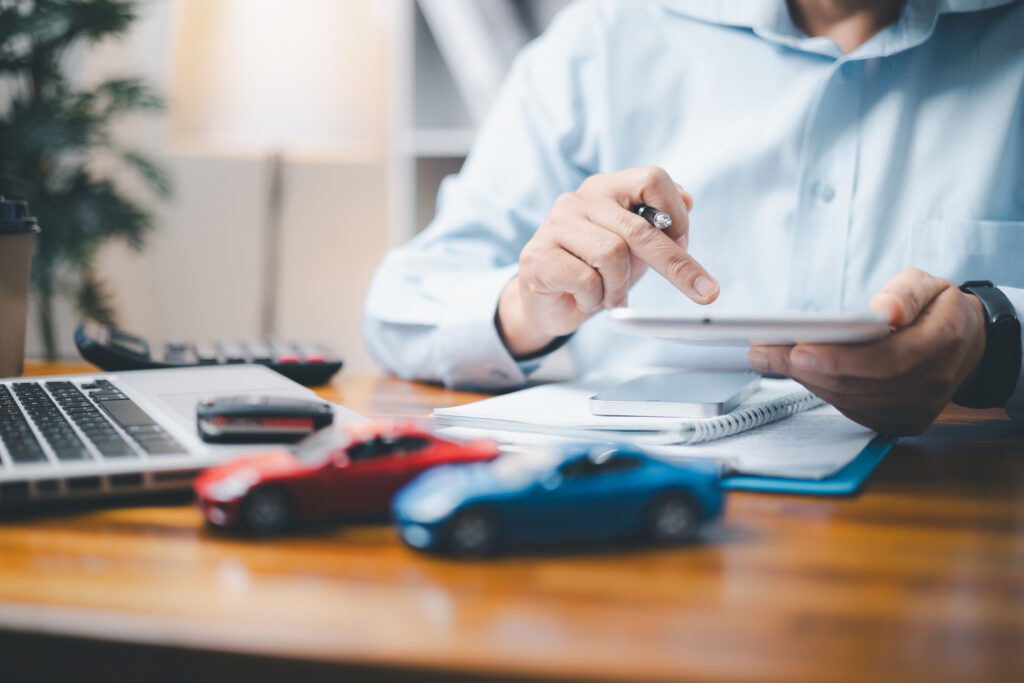 Man reviewing policy and Geico car insurance reviews on a tablet with toy cars and laptop on desk.