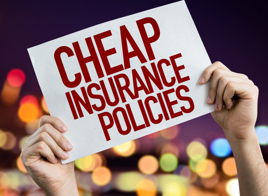 Hands holding a sign that reads "Cheap Insurance Policies" against a blurred city lights background.