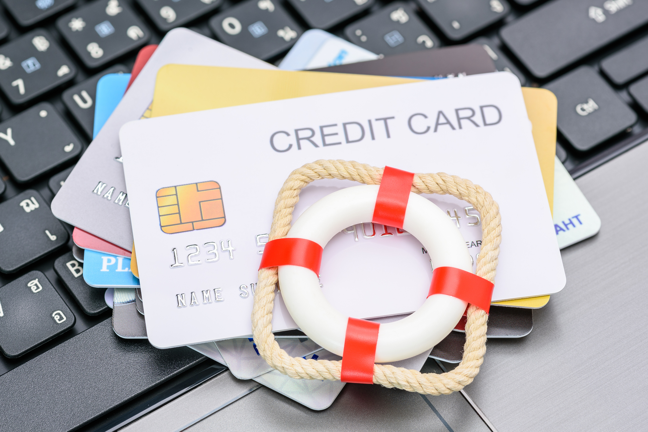 Stack of credit cards on a laptop keyboard with a small life preserver on top, symbolizing debt consolidation vs bankruptcy as financial lifelines.