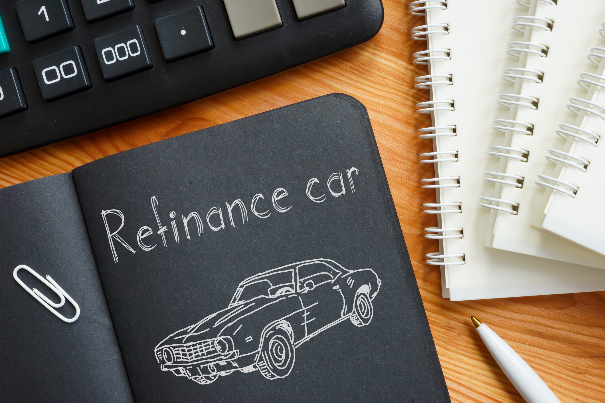 Notebook with &ldquo;Refinance car&rdquo; sketch beside a calculator and pen, representing planning for an auto refinance loan.