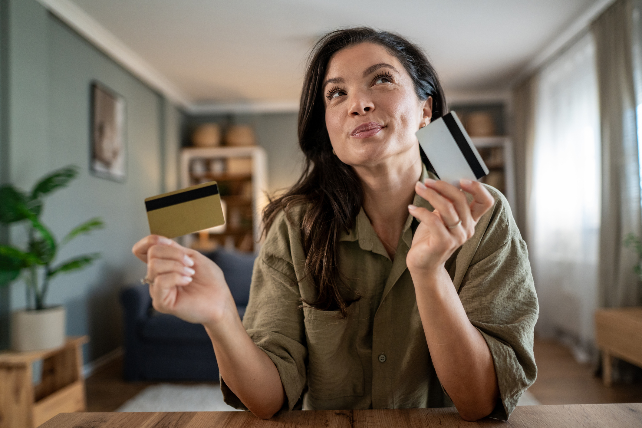 Woman sitting at a table holding two credit cards, considering how many credit cards she should have for good credit management.