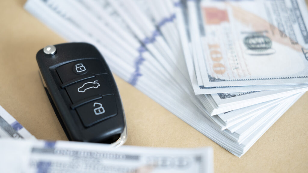 Car key and stacks of hundred-dollar bills representing savings from a Gravity Lending review auto refinance.
