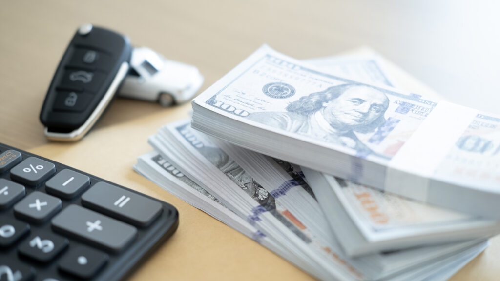 Stacks of cash, car keys, and a calculator representing financial planning for an Ally auto loan review.