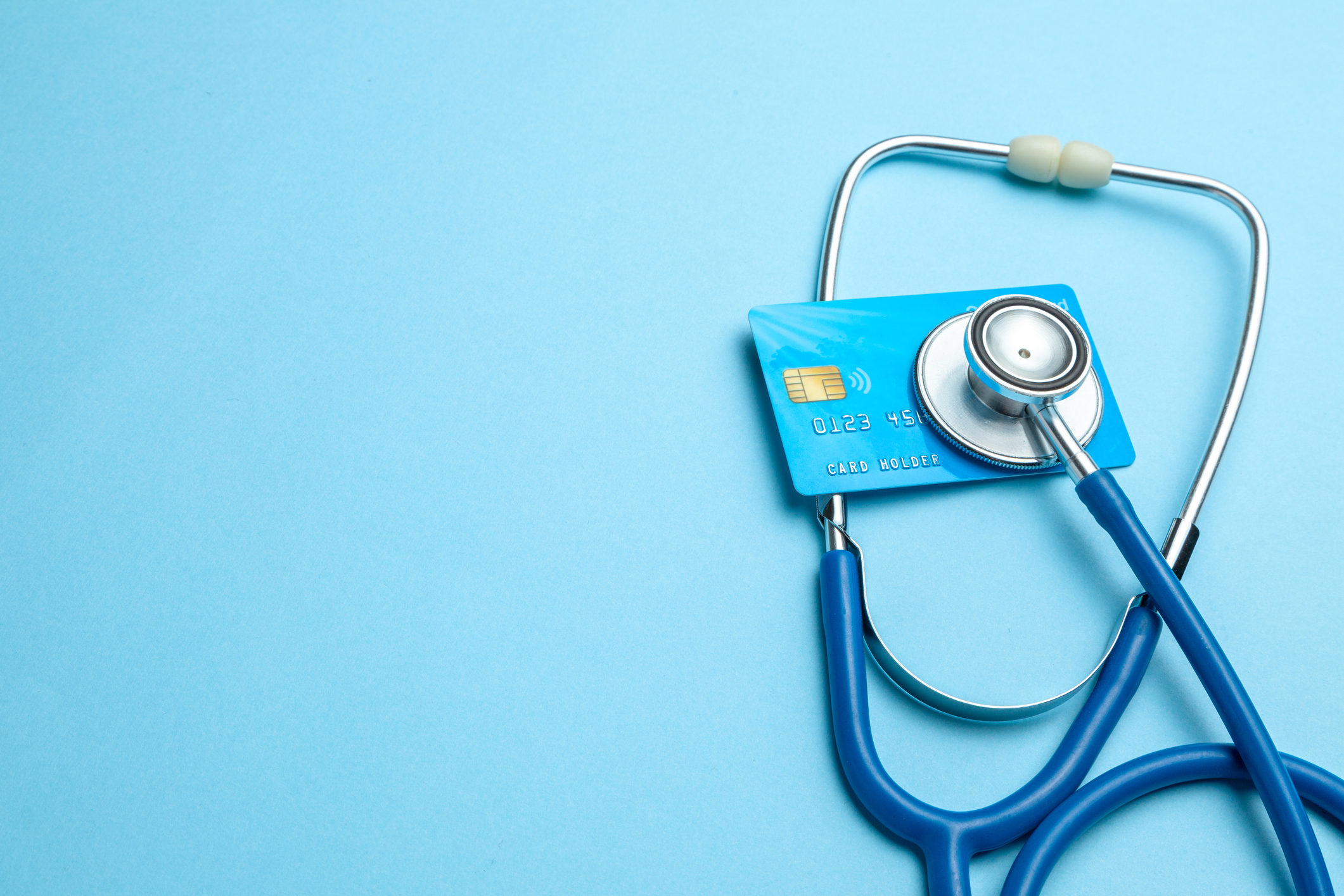Credit Card and Stethoscope Symbolizing Medical Debt A stethoscope pressed against a blue credit card on a light blue background, symbolizing using credit to manage or pay off medical debt.