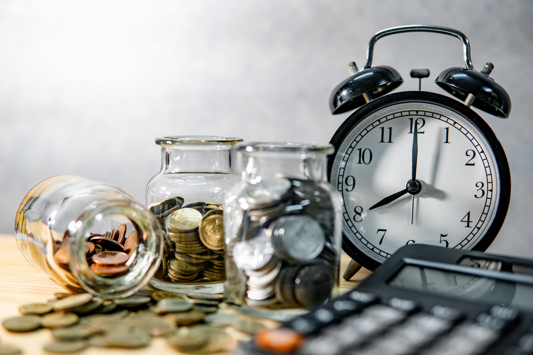 Coins in jars beside a clock and calculator, symbolizing saving time and money with an early loan payoff calculator.