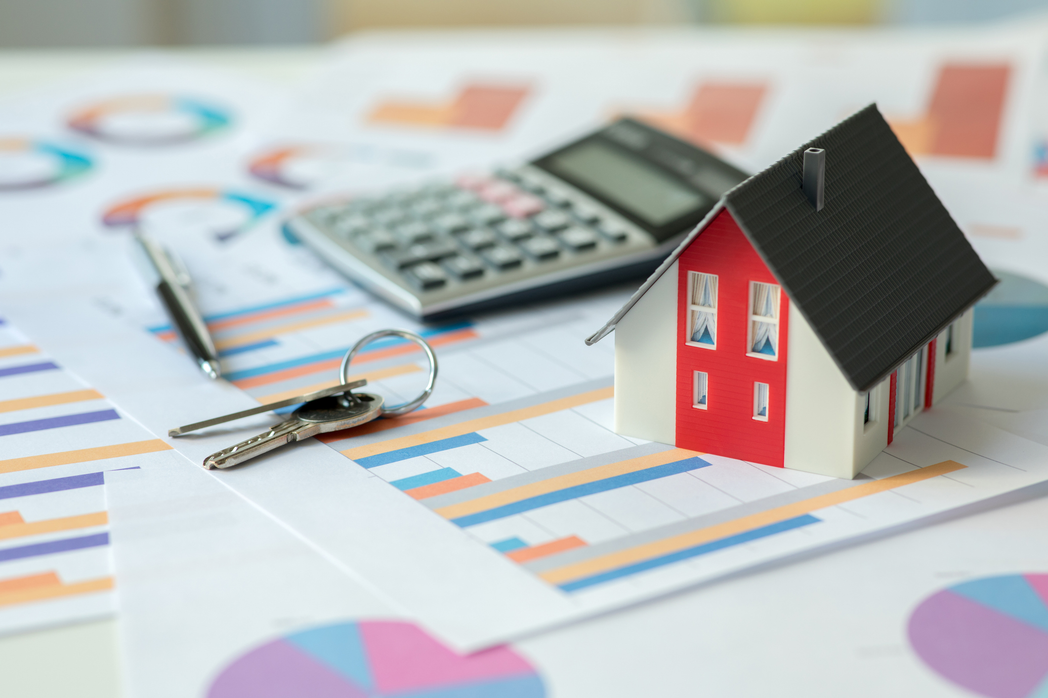 Miniature house, calculator, financial charts, and house keys on a desk symbolizing how debt consolidation affects buying a home.
