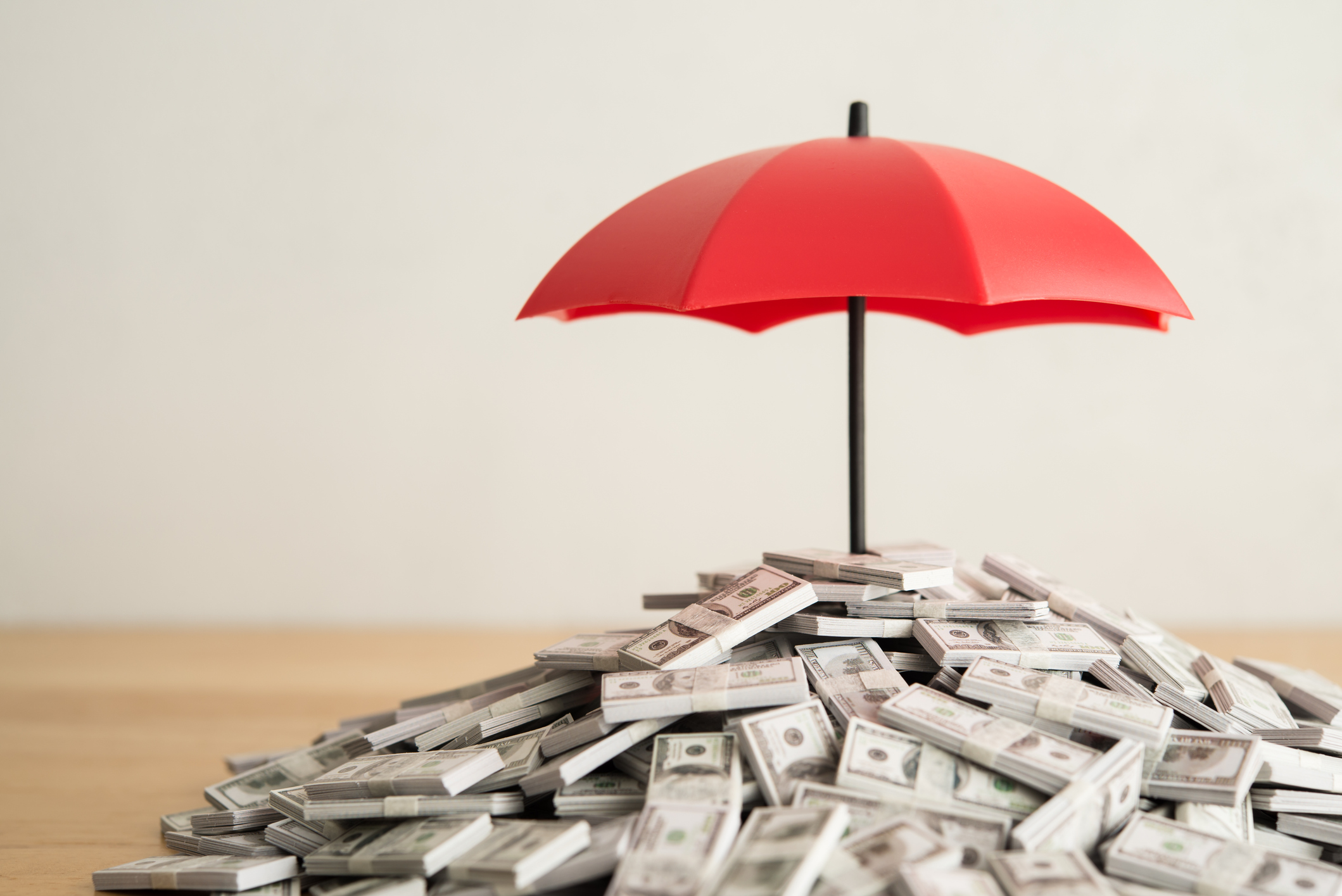 Red umbrella protecting a pile of money, symbolizing financial security and insurance coverage.