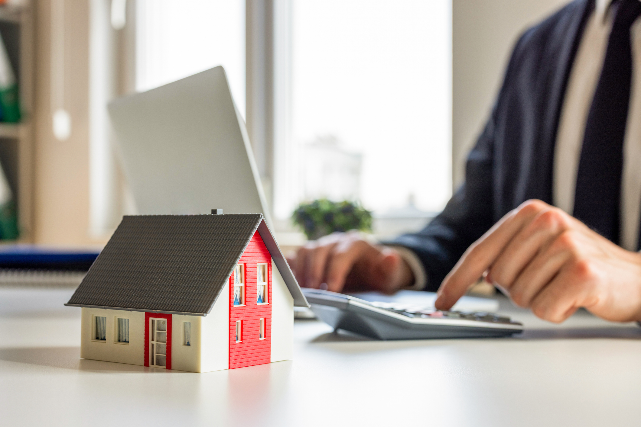 Person using a calculator next to a small model house, representing how a home equity loan calculator helps estimate monthly payments and borrowing limits.