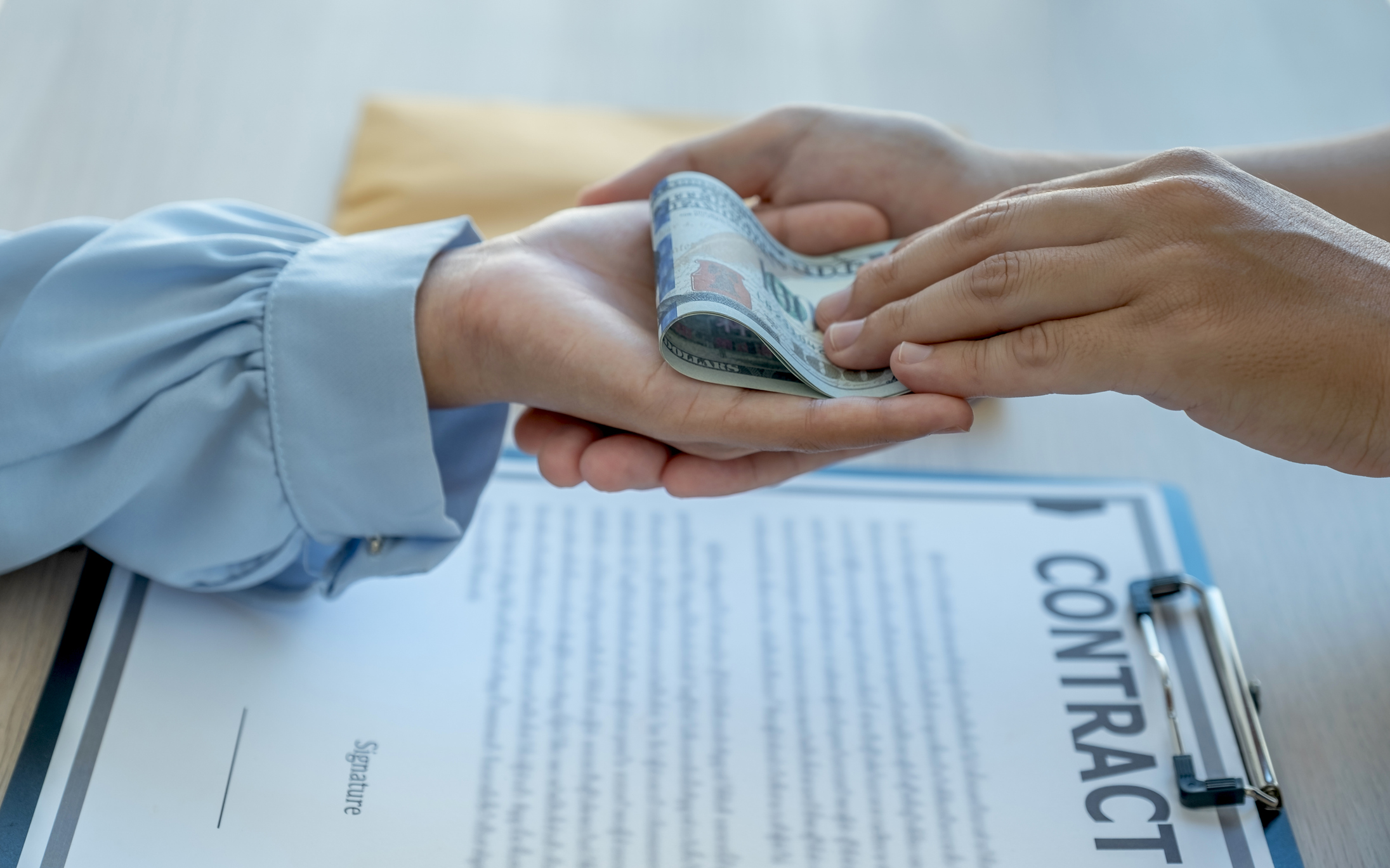 Factors to consider when borrowing money, shown by a cash exchange over a signed loan contract.