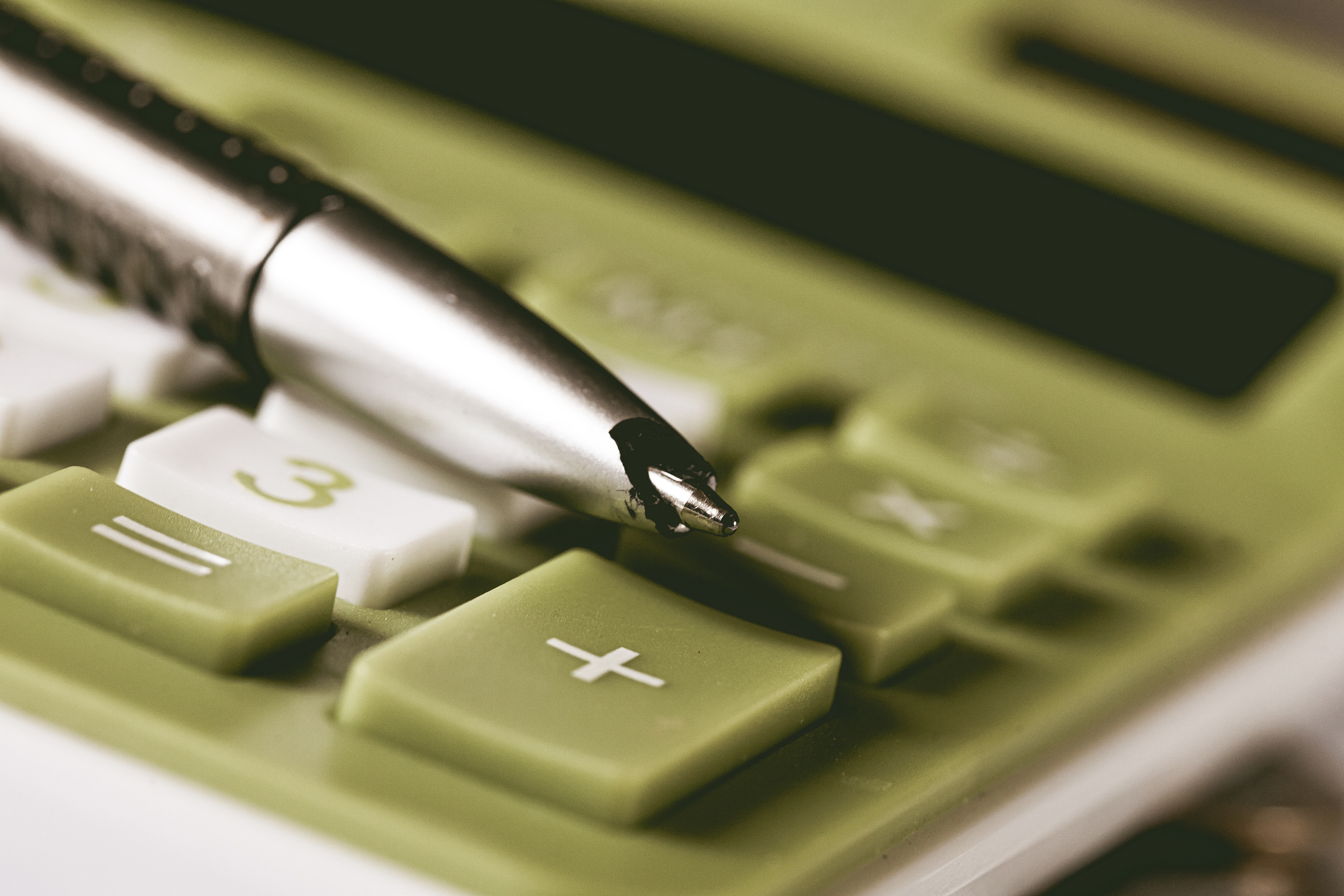 Close-up of a pen resting on a calculator, representing the use of a debt consolidation calculator.