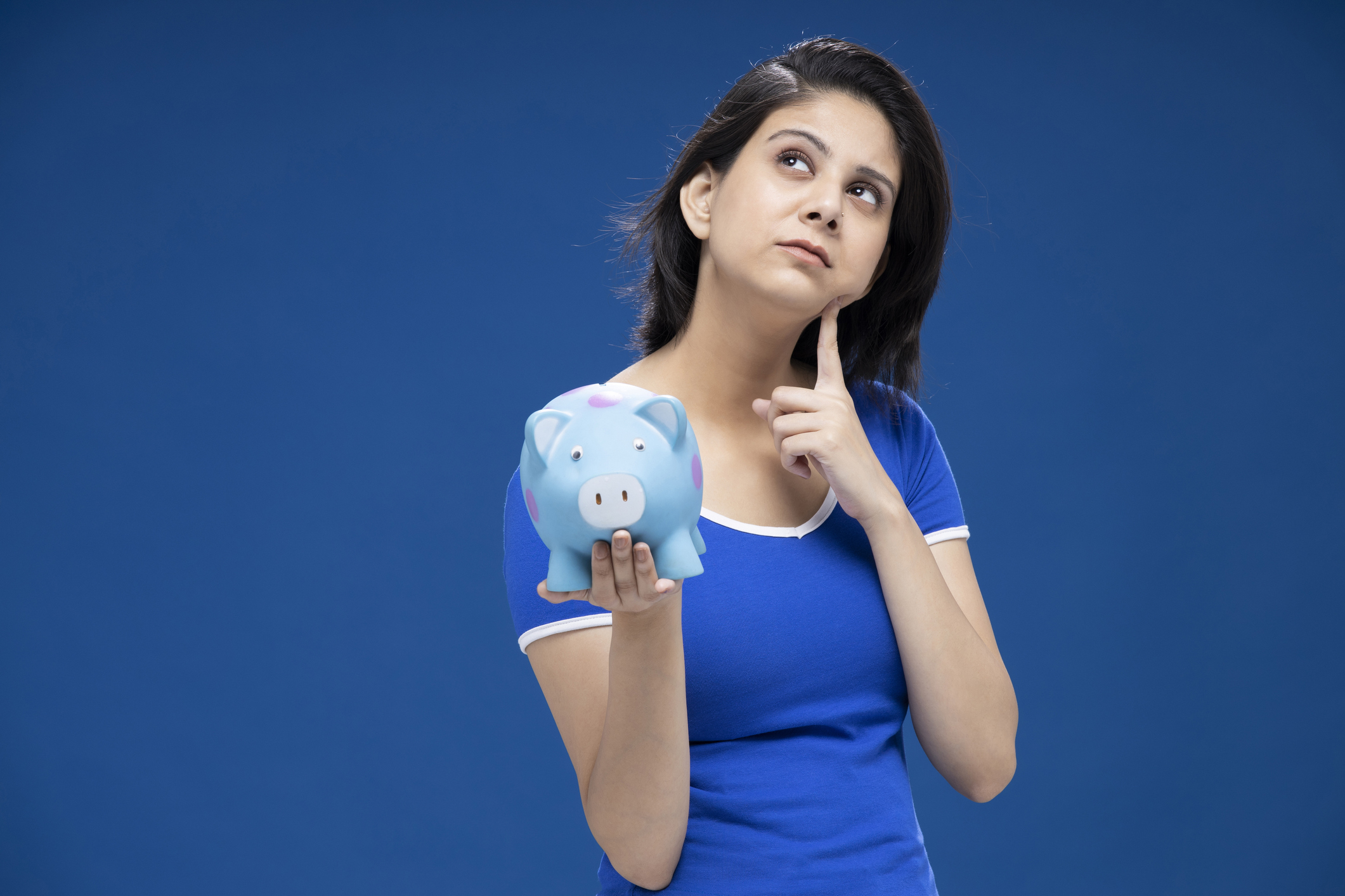 How Much Should I Be Saving? Realistic Savings Goals Explained How much should I be saving? A woman holds a piggy bank while thinking about realistic savings goals.