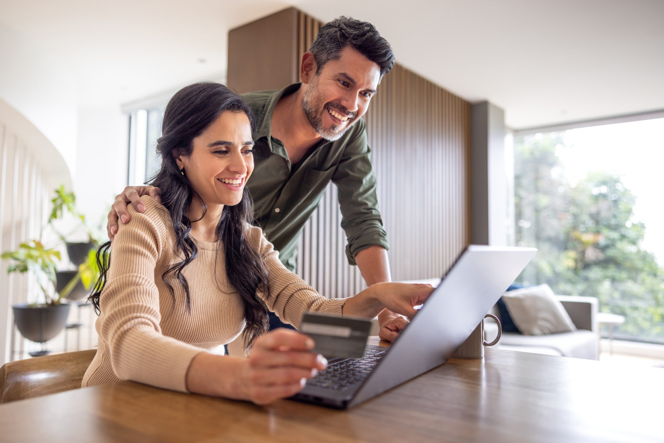 Couple using a credit card for an online purchase on a laptop at home